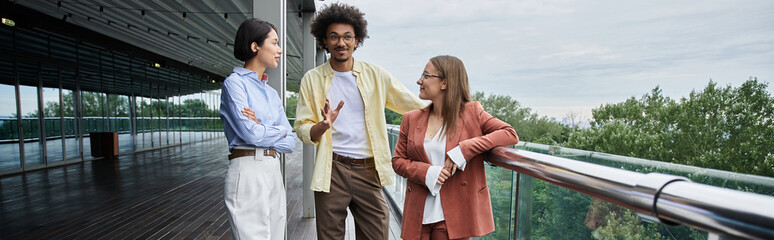 Three colleagues stand on a rooftop terrace, chatting and laughing.