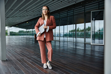 A woman with a prosthetic leg stands on a modern office terrace with a laptop in hand.