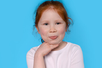 Naklejka premium Young Redhead Girl Sticking Tongue Out In Front Of Blue Background