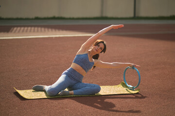 focused pose, the woman in blue sports gear executes a V-sit with a fitness ring on a sunny track....