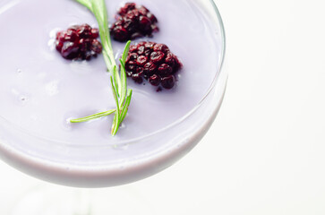 A glass of purple liquid with blackberries floating on top