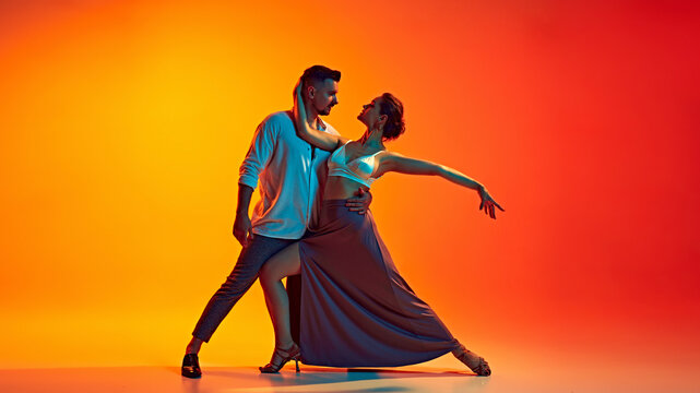 Dynamic dance duo. Romantic and passionate man an woman dancing bachata against gradient yellow orange background in neon light. Concept of dance, performance, art, entertainment