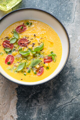 Gazpacho made of sweet corn, yellow tomatoes and bell peppers, vertical shot on a grey and beige granite background, elevated view, middle closeup