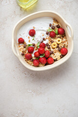 Breakfast yogurt and strawberry bowl on a light-beige stone background, vertical shot with copy space, top view