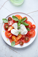 Caprese with buffalo mozzarella, tomatoes and green basil leaves, vertical shot on a white granite background, elevated view