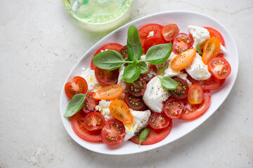 Caprese salad with torn mozzarella, tomatoes and fresh green basil, horizontal shot on a beige stone background, high angle view