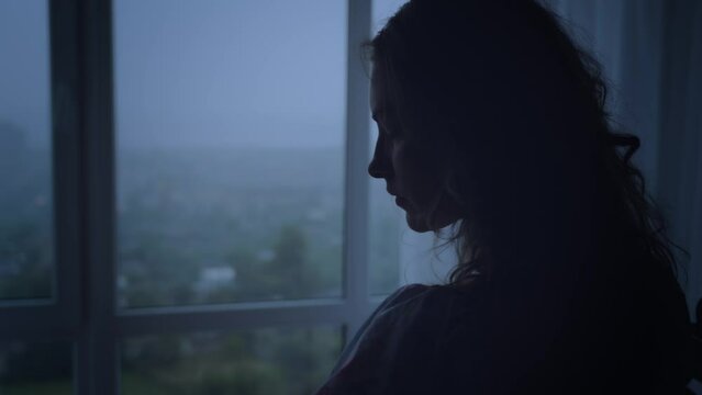 black dark silhouette of young woman crying looking at window rain drops falling rainy weather mood depression sadness loneliness emotion back view. Adult Girl sad tear-stained face. video footage 4k