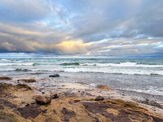 Beautiful Lake Superior landscape, morning light in a cloudy sky over teal blue waters and waves crashing on the rocky lakeshore