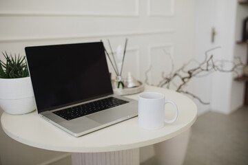 Laptop and white mug with tea on a table. Workspace in a modern room.