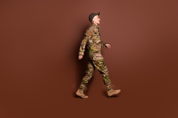 Full size photo of pretty senior female brave servicewoman walk profile wear camouflage military uniform isolated on brown color background