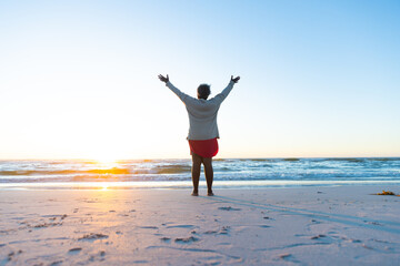 A senior African American woman enjoys a serene beach sunrise, with copy space