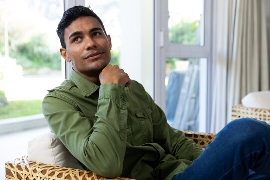 Young biracial man sits thoughtfully in a home setting, unaltered - Powered by Adobe