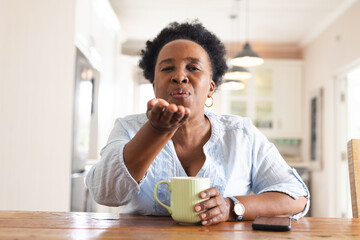 Portrait of happy senior african american woman blowing kiss and having video call at home