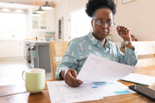 Busy senior african american woman wearing glasses and reading documents on table at home - Powered by Adobe