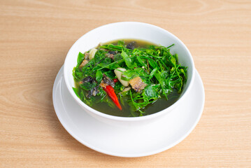Plant of family Euphorbiaceae in soup. Northern Thai food (Kang Pak Wan), Spicy local Thai vegetable soup with dry fish in a bowl on wooden table background, Thai local street food, Thai food-Top view