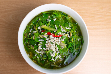Thai food Melientha suavis plant in soup with red ant egg. Famous green leaves food in white bowl on wooden table, top view background. Local ingredient vegetable, red ant eggs, topview