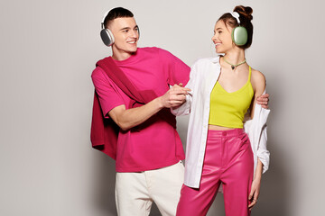 Obraz premium A fashionable man and woman, wearing headphones, stand next to each other in a studio with a grey background.