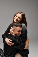A man and a woman intertwine in a warm hug, expressing affection and closeness in a studio with a grey backdrop.