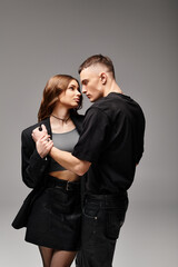 A young couple, standing close together, exuding love and connection in a studio against a grey background.