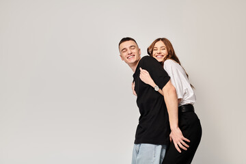 A man and woman, young couple, hugging each other affectionately in a studio with a grey background.
