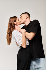 A young man and woman share a passionate kiss in a studio with a grey background.