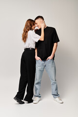A young couple, deeply in love, stands side by side in a studio against a grey background.