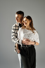 A young couple in love standing side by side in a studio with a grey background.