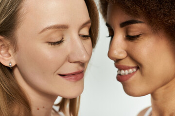 Two women, close together with eyes closed and lips parted, share a tender moment against a grey backdrop