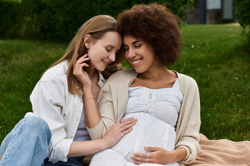 A pregnant woman and her partner share a tender moment in a green grassy field, their hands resting on the growing belly.