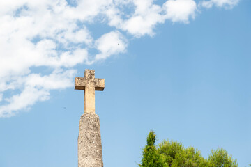 imagen de una cruz de piedra, con el cielo azul y algunas nubes en el cielo 