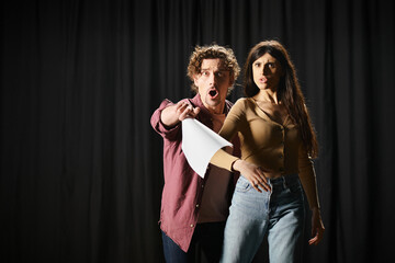 A stylish man and woman pose confidently in front of a black curtain during theater rehearsals.