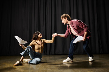 A handsome man kneels beside a woman on the floor in a theatrical setting.