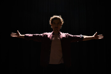 A man stands with arms outstretched in darkness.