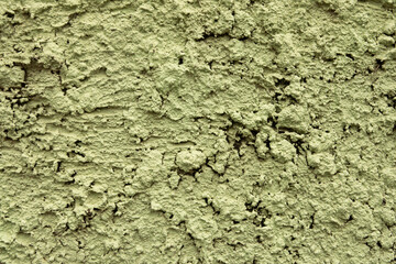 A wall with a greenish color and a rough texture. The wall has a lot of cracks and holes, giving it a worn and aged appearance