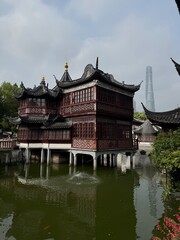 Fototapeta premium Historic Pavilion Overlooking Serene Pond at Yu Garden with Modern Shanghai Skyline in Background