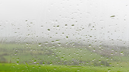 A window pane, dotted with rain, overlooks verdant scenery.