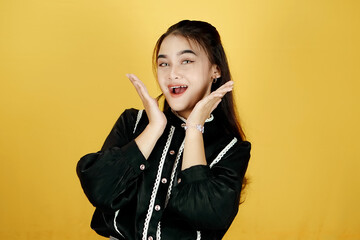 Fototapeta premium Young Indonesian woman standing confidently, her charming smile highlighting her beauty, on isolated yellow background