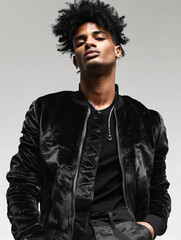 Obraz premium fashion studio photo of an afro american man wearing black velvet jacket, posing on grey background, low angle view from below, hands in pockets,