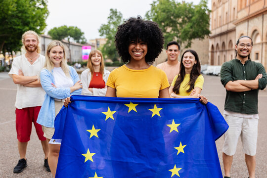 Diverse group of people holding European Union Flag while smiling at the camera standing together outdoors