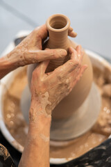 Close-up of a potter's hands making a ceramic vase on a potter's wheel. 