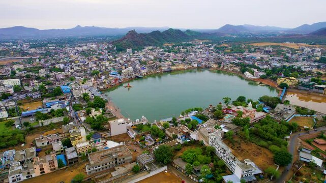 aerial drone panning distance shot showing pushkar lake, colorful buildings, temples, ghats and the aravalli hills covered with fog in the distance showing the cityscape Rajasthan India