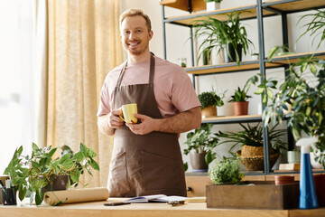 A handsome man in an apron enjoys a cup of coffee in a plant shop, embodying the essence of owning a small business.