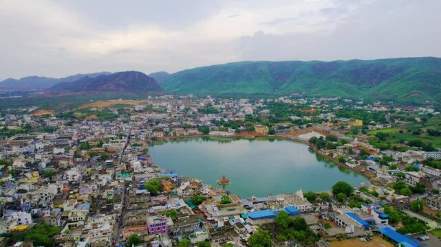 dusk aerial drone shot flying towards pushkar lake cityscape showing colorful buildings with lights and aravalli hills in the distance showing holy town in rajasthan India