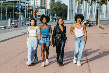 Fototapeta premium Diverse young women are strolling side by side down a wide city sidewalk.