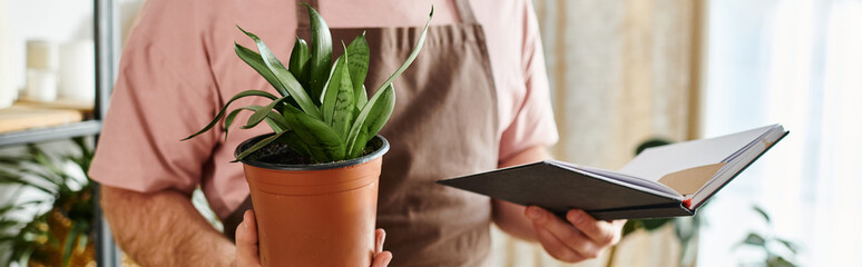 A cropped man holding a potted plant and a notebook.