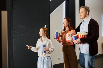 A happy family stands close, holding popcorn in a cinema setting, enjoying a cheerful moment together.