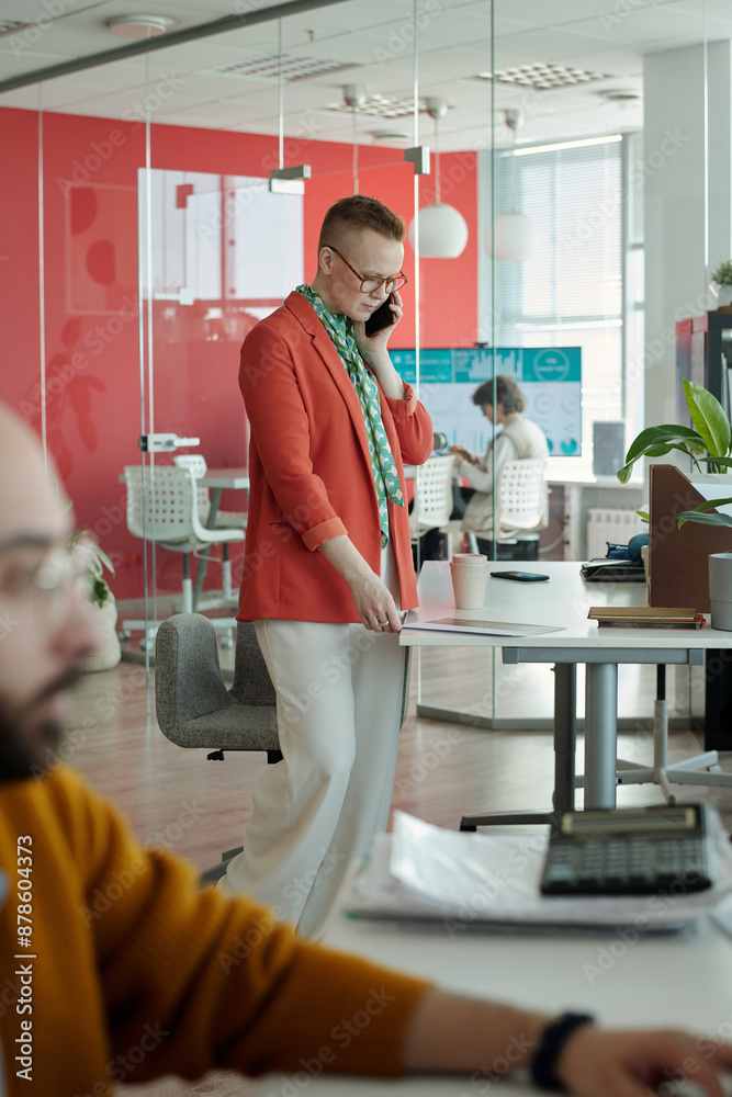 Wall mural professional businesswoman engaging in conversation on smartphone while standing in modern office, w