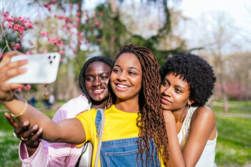 Three happy African women taking a selfie together in a sunny park.