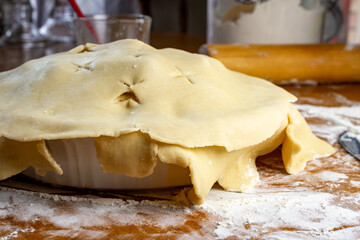 Making a pie:  Top crust.  Dough is unfolded with edges hanging over the side of the prepared apple pie.