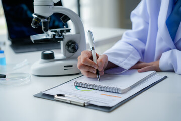 Scientist in lab coat documenting research findings with microscope in background, representing science and medicine concept